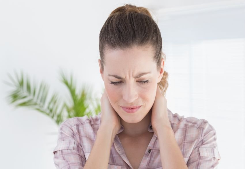 Woman holding her neck due to stiffness and discomfort associated with chronic headaches.