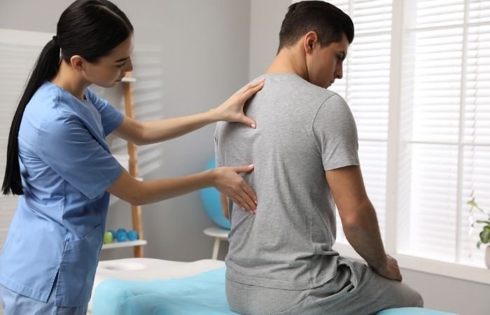 Physiotherapist examining a seated patient's lower back during a sciatica assessment
